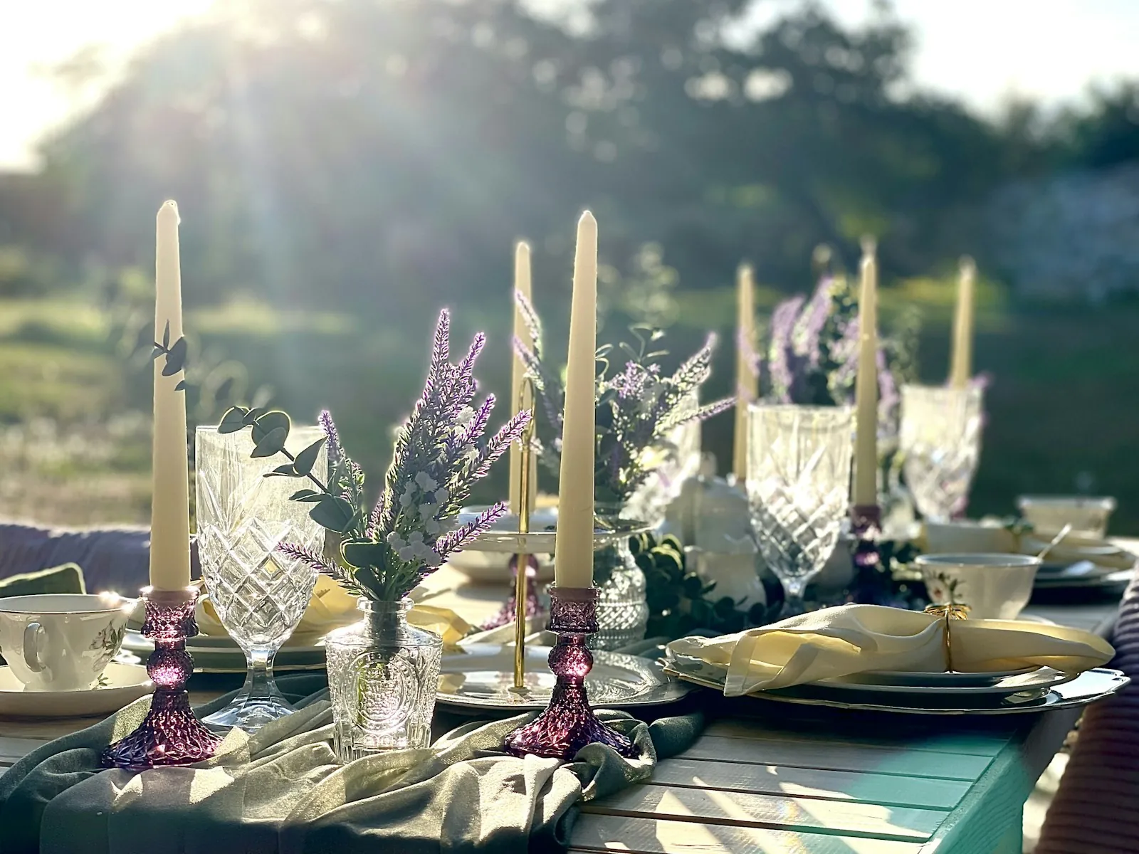 Una mesa decorada con velas, cristalería y lavanda, preparada al aire libre